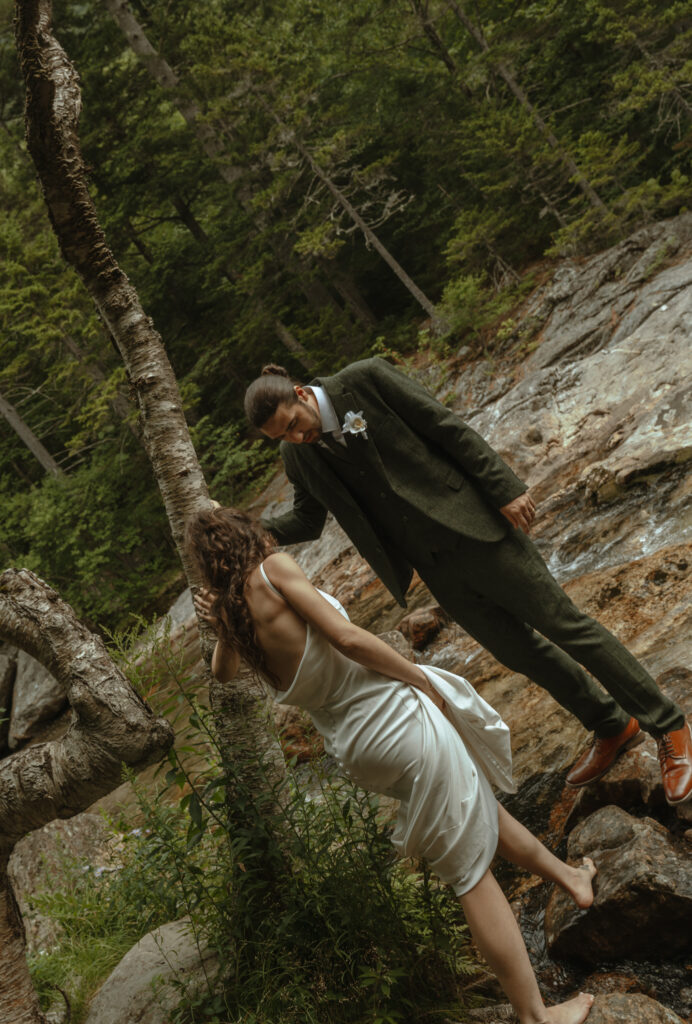 Couple walking over wet rock at the base of a New Hampshire Waterfall for their elopement.