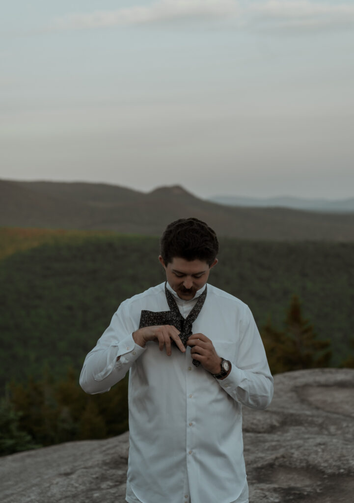Groom putting his tie on before his first look during his sunrise white mountain elopement