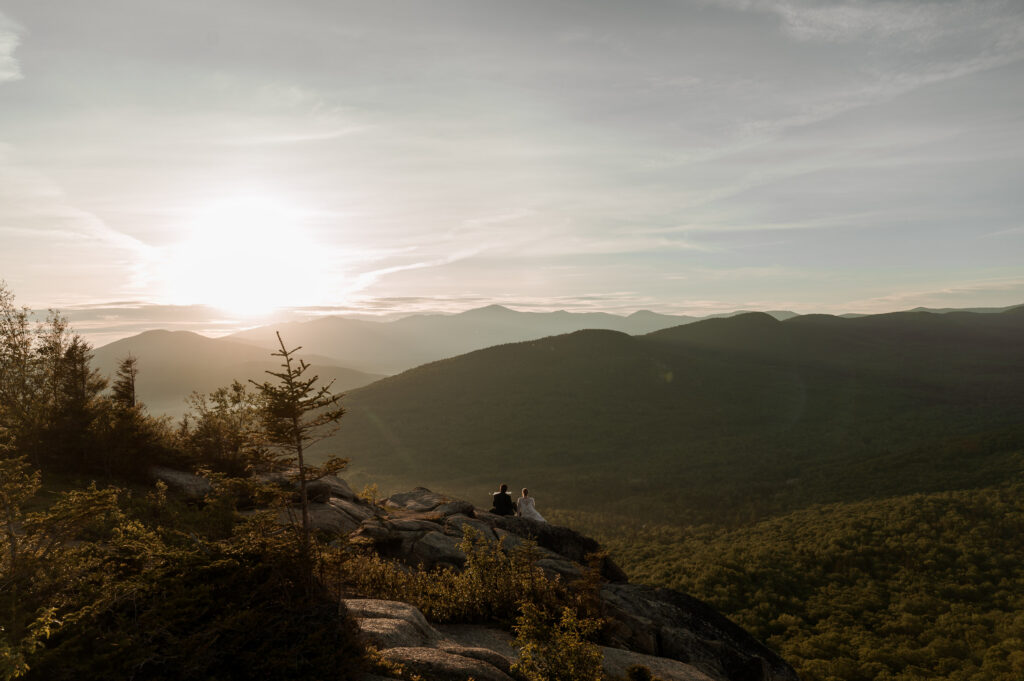 Bride and groom watching sitting at the mountain top during their sunrise elopement in the White Mountains of New Hampshire